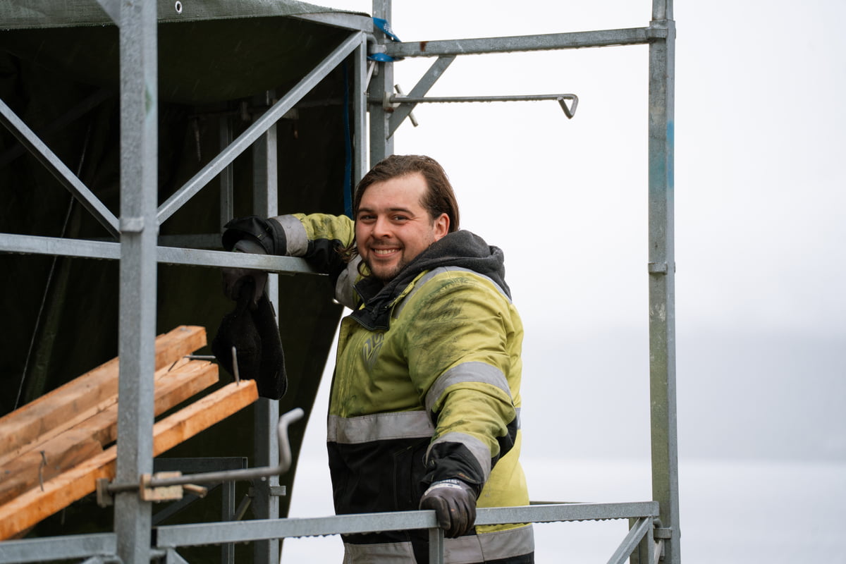 En håndverker står i et stillas og smiler