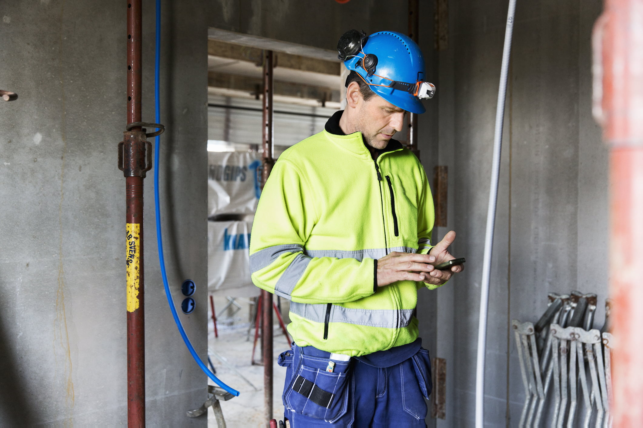 Byggearbeider med hjelm og arbeidsklær sjekker mobilen.