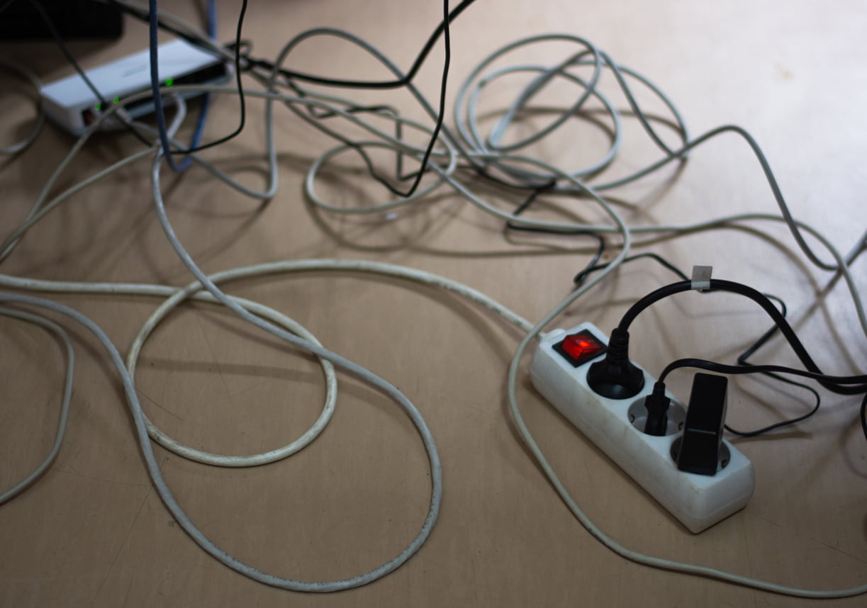 Et virvar av kabler og en skjøteledning på et lyst tregulv
