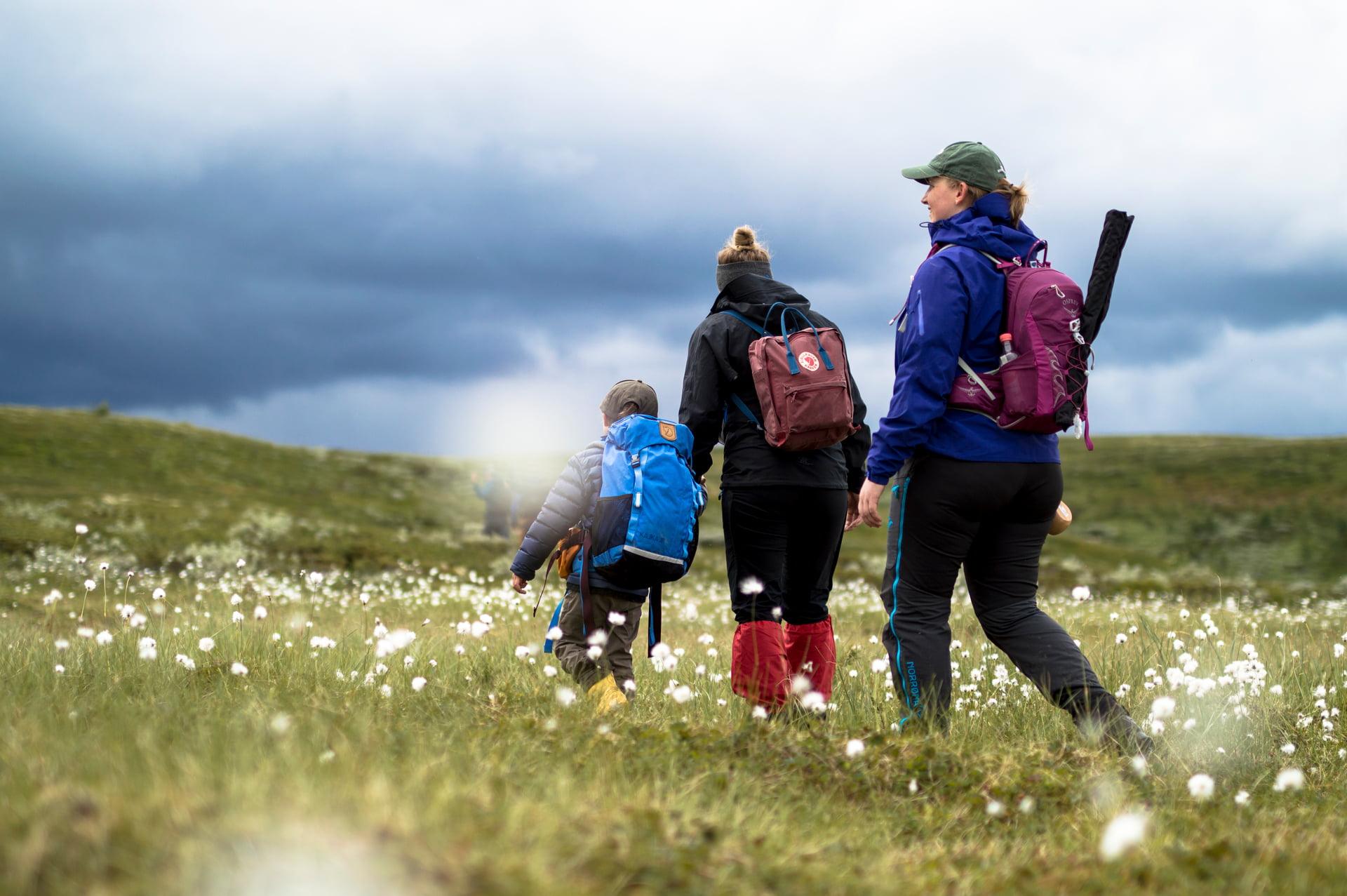 To kvinner og et barn går gjennom en myr med fiskeutstyr