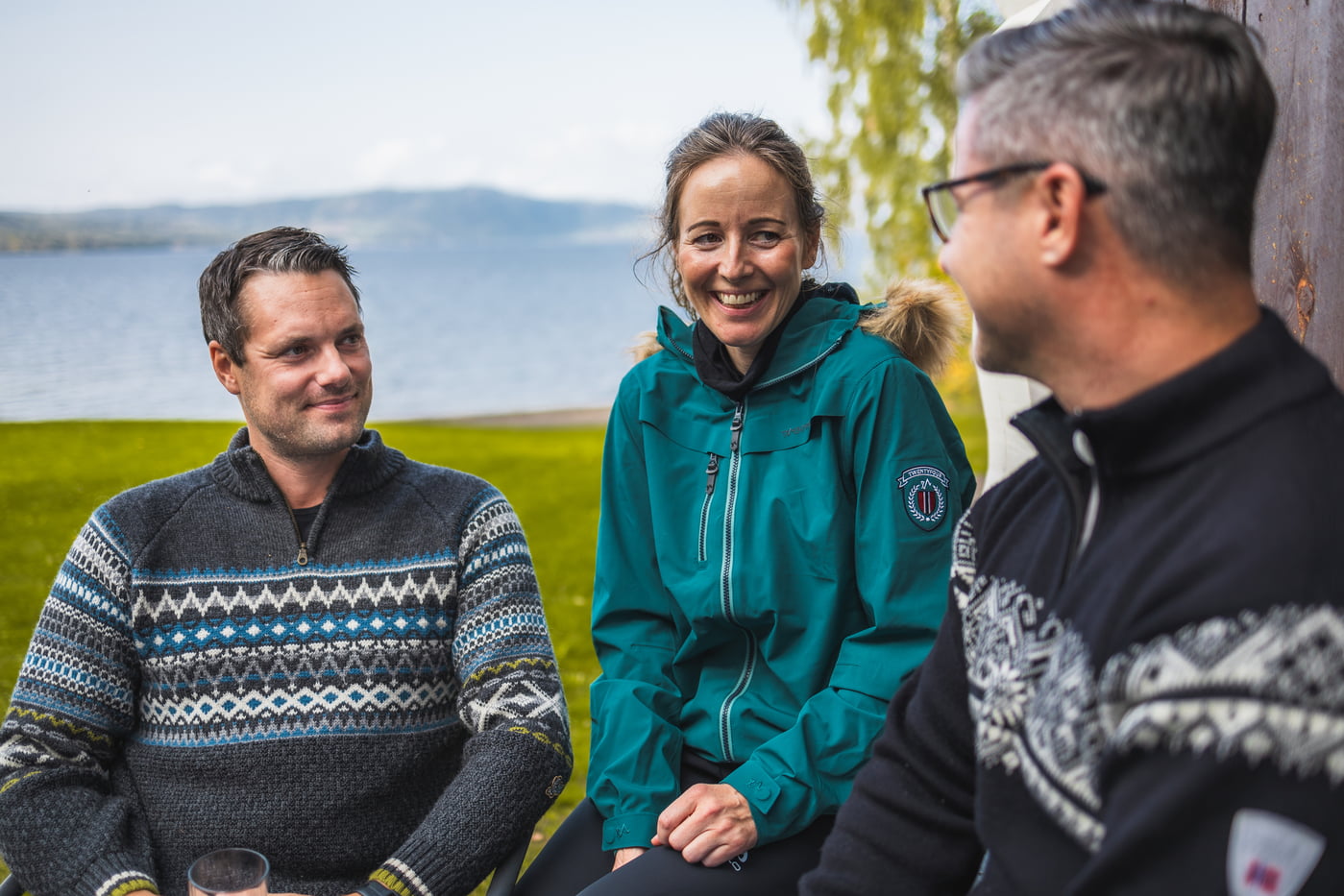 To menn og en kvinne sitter i hytteveggen foran et vann 