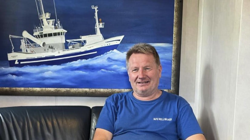 Skipperen i lugaren foran et bilde av baten