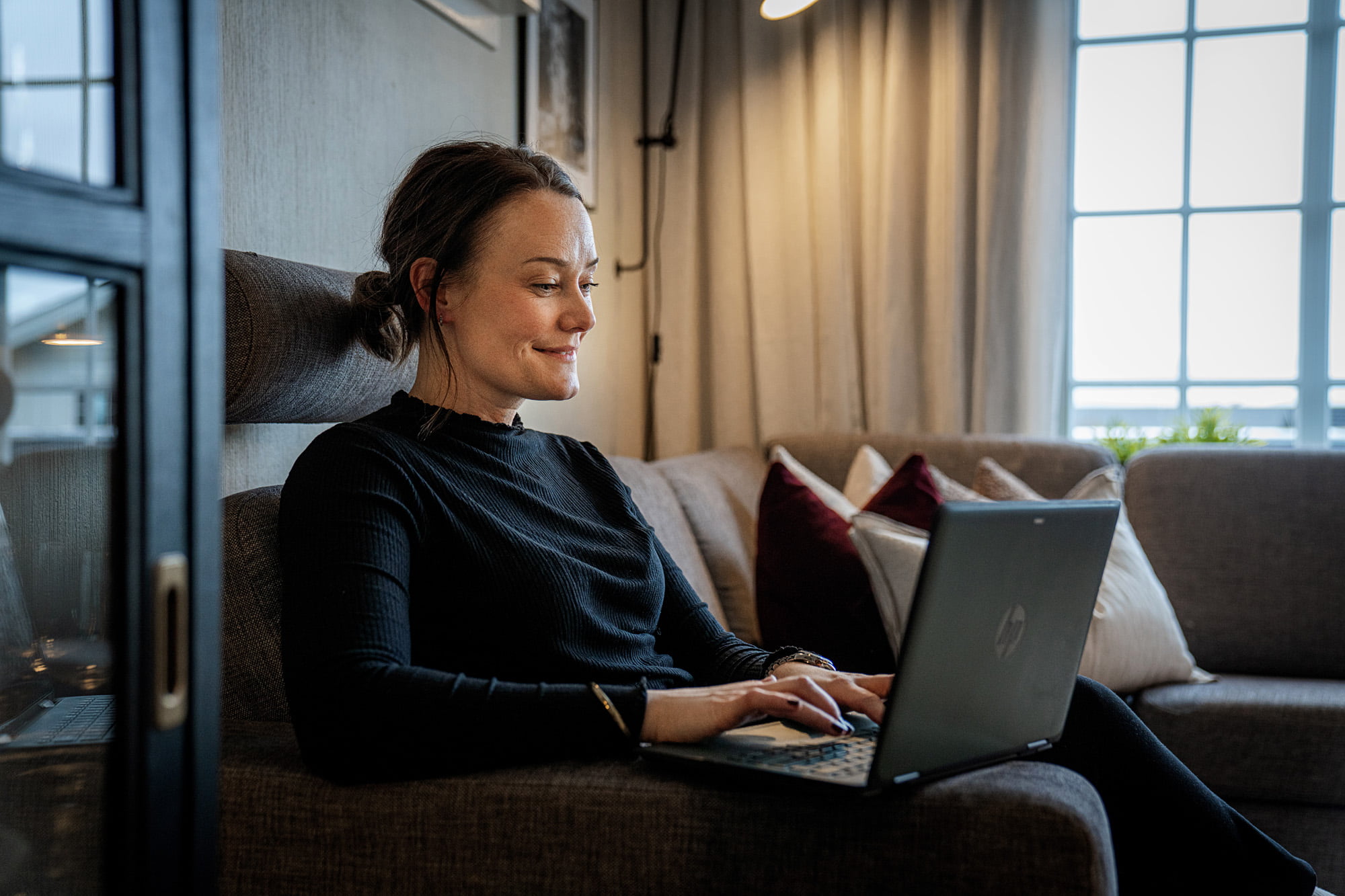 En kvinne sitter i sofaen og jobber på en laptop