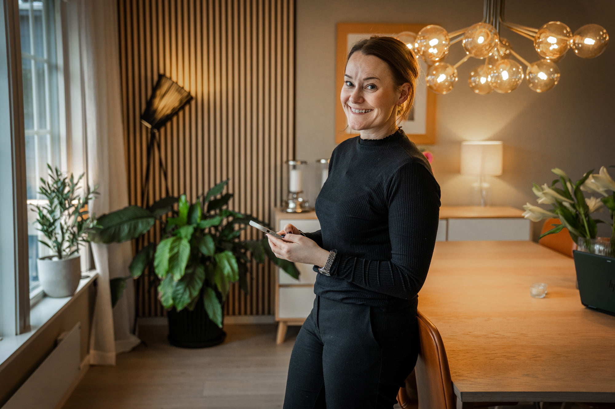 En kvinne står ved spisebordet og smiler til kameraet 